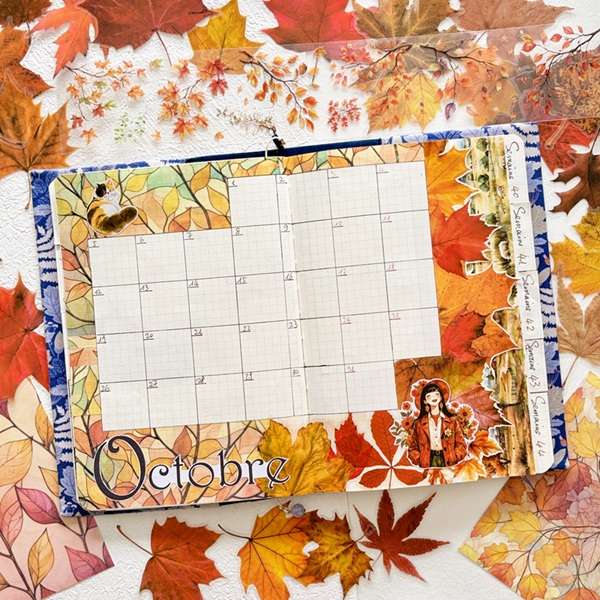 Carnet de journaling ouvert sur un calendrier d’octobre, décoré de stickers automnaux, de feuilles colorées et de masking tapes pour le scrapbooking et la papeterie créative.